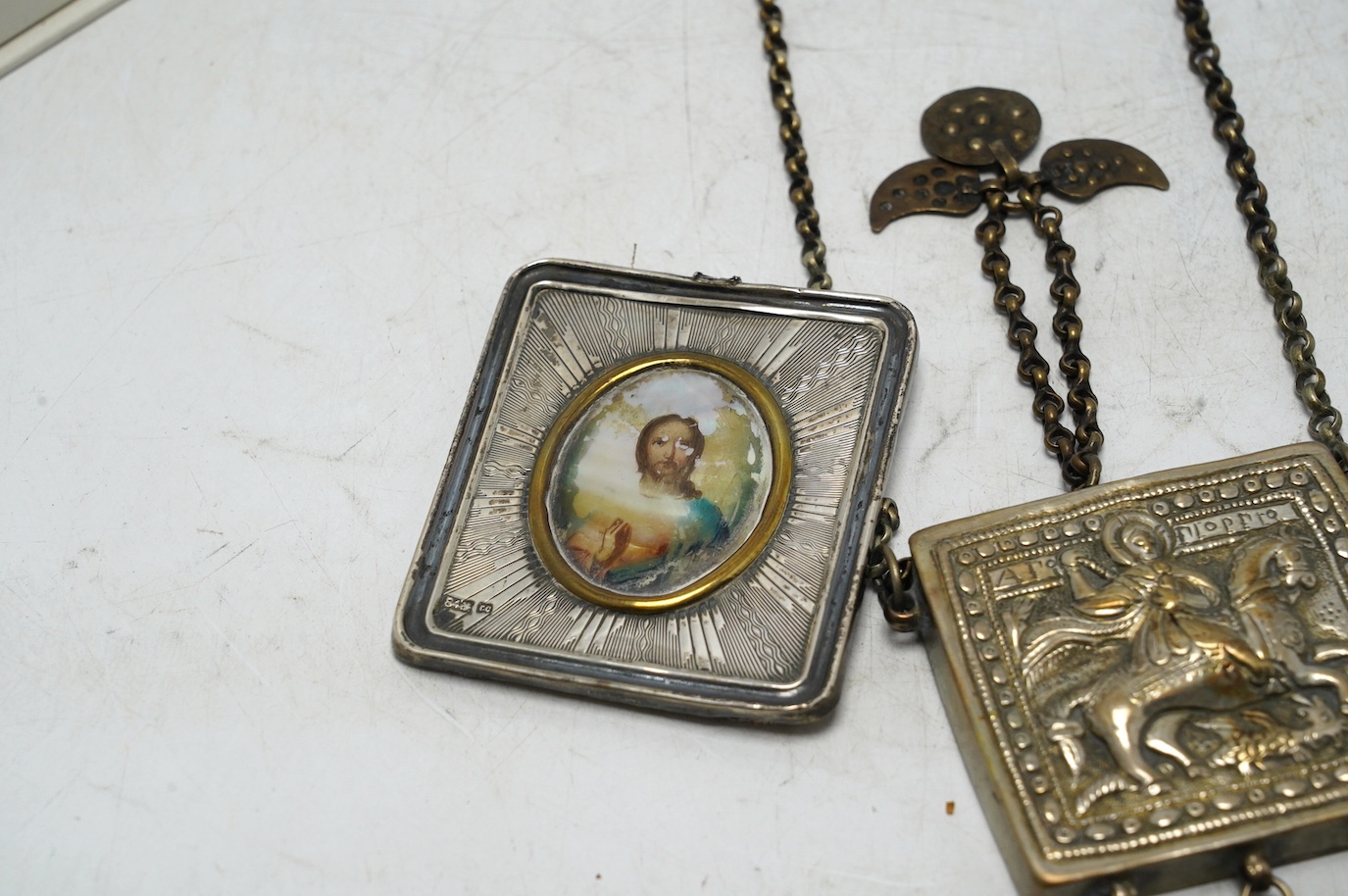 A Greek white metal pendant, embossed with St. George and the dragon, on a chain and a Russian white metal framed portrait of Christ. Condition - poor to fair